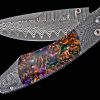 The Spearpoint 'Big Easy' features a beautiful frame in 'River Rock' damascus by Chad Nichols, inlaid with mini pine cones in resin. The blade is 'Wave' pattern damascus steel with an extra-strong core of ZDP-189. The one-hand button lock and the thumb stud are set with smoky quartz gemstones. A remarkable design that gives you an instrument with a full-size secure grip, and a versatile deep-belly blade, the Spearpoint epitomizes William Henry’s core philosophy – that superlative function deserves to be elevated to superlative art. The 'Big Easy' also features William Henry's most admired and distinctive forged metals; a timeless heirloom to be proudly worn and used for a lifetime before being handed-down to another generation
FEATURES & SPECS
One-hand button lock system

Dimensions:

Blade 3.06" (77.7mm)
Handle 4.13" (104.9.5mm)
Overall open 7.19" (182.6mm) - Image 3