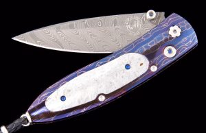 The Monarch 'Halley' features a beautiful frame in hand-forged, heat-blued 'Croc Skin'' damascus by Chad Nichols, inlaid with a mesmerizing meteorite scale (a section of the Gibeon meteorite which fell in the desert of Namibia in prehistoric times). The blade is hand-forged 'Boomerang' damascus also by Chad Nichols. The one-hand button lock and thumb stud are set with sapphire gemstones.
The Monarch is a simple design that is easy on the eye and effortless in the hand. The 'Halley' features some of William Henry's signature forged metals, and represents the perfect synthesis between elegance, function, modern and exotic materials; a distinctive personality statement to be worn and used for a lifetime.
Features & Specs
One-hand button lock system
Leather carrying case
Shipped in an elegant wood presentation box
Dimensions: 
Blade 2.63" (66.8mm)
Handle 3.58" (90.9mm)
Overall open 6.00" (152.4mm)
40 of 50